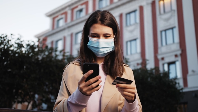 Womn outside holding a smartphone and a credit card, symbolizing the rise of mobile-based spending during the pandemic era.
